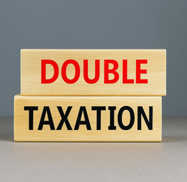 A pair of wooden blocks stacked on a grey surface with the top block displaying the word DOUBLE in red capital letters and the bottom block showing TAXATION in black capital letters, symbolising the concept of double taxation.