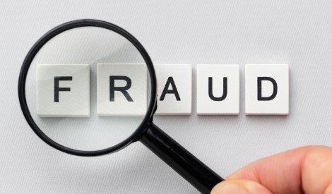 Magnifying glass focusing on the word FRAUD spelled with white letter tiles, symbolising fraud detection and prevention.